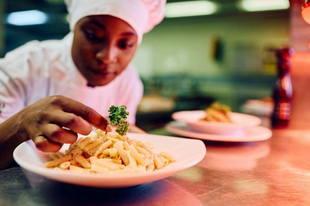 Close up of black female chef serving a dish in restaurant kitchen.