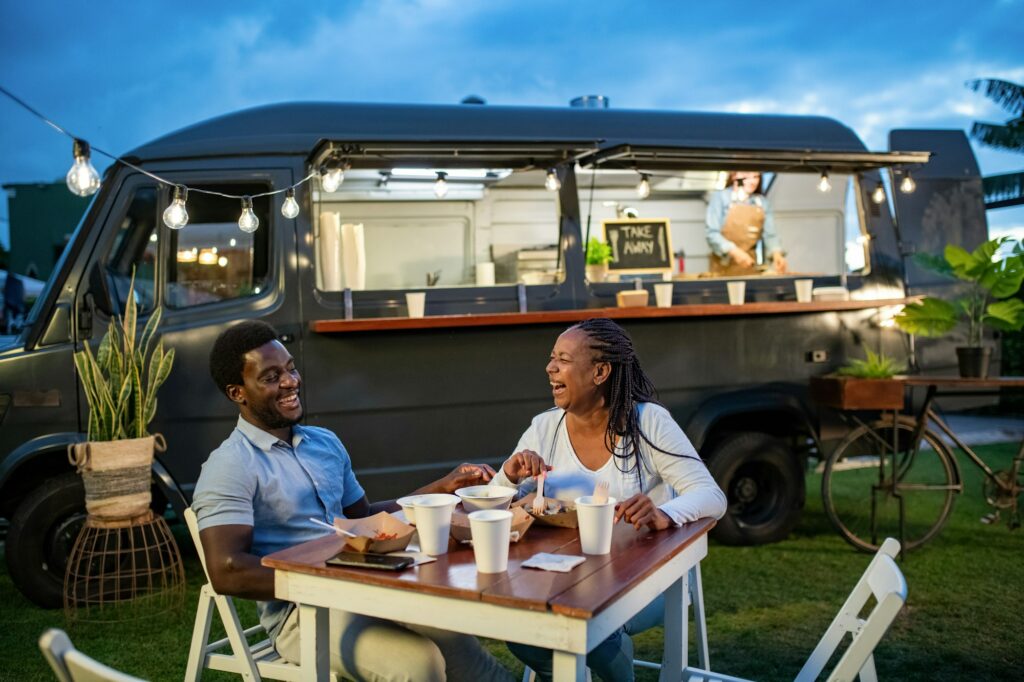 Happy black couple eating near food truck in evening